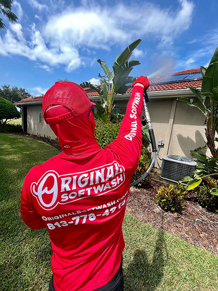 Tech in a red Original Softwash hoodie soft washing a stucco house