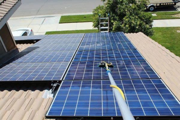 Solar panels being cleaned with a soft brush on a pole