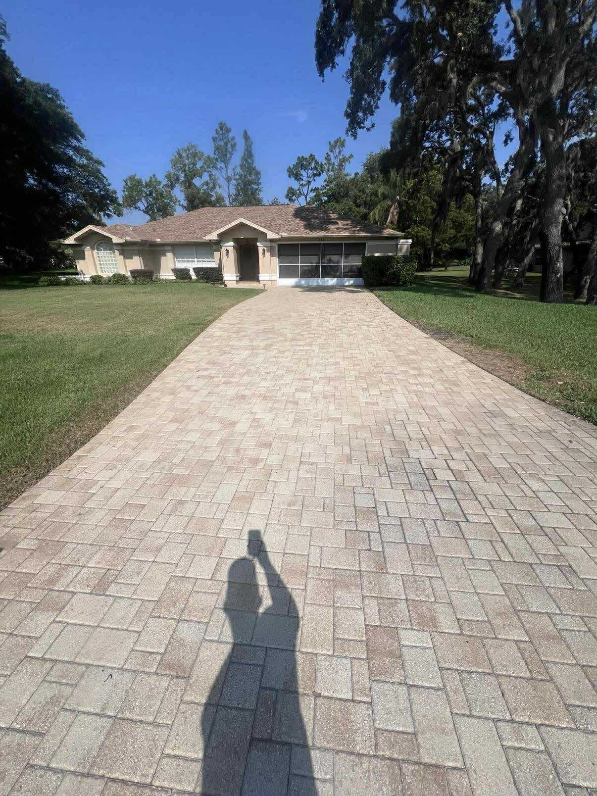 Long tan paver driveway running up to a single-story home under oak trees